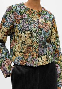 Veste à motif floral présentant une variété de couleurs, notamment du jaune, du rose et du bleu ; tissu texturé avec un col rond et des manches longues.