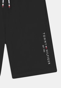 Černé bavlněné šortky s bílým vyšitým logem "TOMMY HILFIGER EST. 1985." Obsahují šňůrku s červenými, bílými a modrými akcenty.