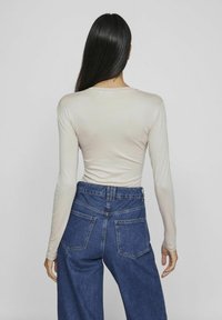 Långärmad beige topp i kombination med högmidjade blå jeans. Toppen har en mjuk textur och en enkel rund halsringning, medan jeansen har bakfickor.