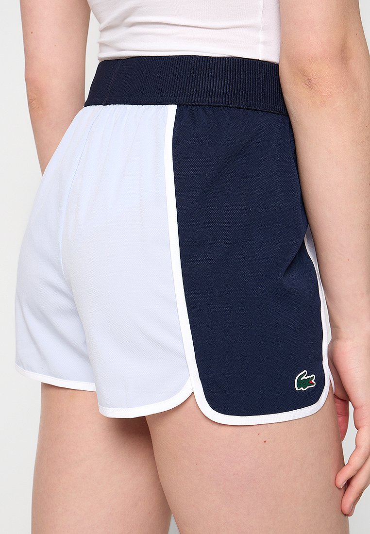 Shorts de sport bleu marine et bleu clair avec une taille côtelée, des bords blancs et un petit logo sur le côté. Texture en maille visible.