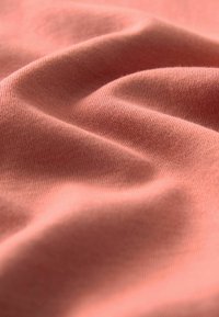 Zacht, soepel fabric in een gedempt koraalkleur, met een fijne textuur en subtiele golvingen die een vloeiende uitstraling creëren.