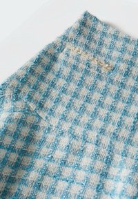 Tela de cuadros azul y blanco con una superficie texturizada, que presenta un borde deshilachado y un sutil detalle de costura en dorado.