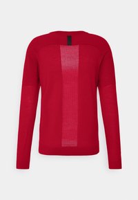 Pull rouge à manches longues avec un motif tricoté perforé vertical au centre du dos et une languette en tissu noire à l'encolure.