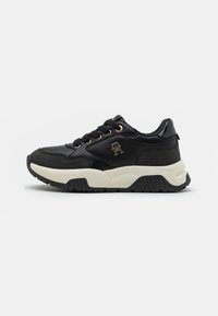 Zwarte sneaker met een textuurstof bovenwerk, gouden accenten, een chunky witte tussenzool en een zwarte rubberen outsole. Beschikt over ronde veters en logo-detail.