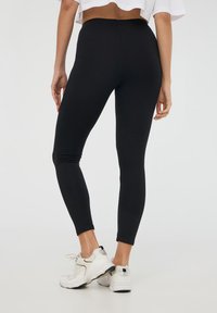 Leggings neri realizzati in tessuto elasticizzato, con una vita alta e una vestibilità affusolata, abbinati a scarpe da ginnastica bianche.