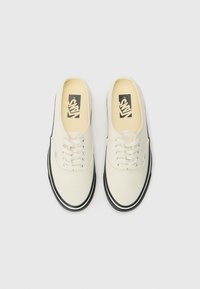 White canvas sneakers with black rubber soles, laces, and iconic logo on the insoles. Rounded toe design and contrasting perimeter stitching.