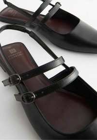 Czarne płaskie buty z ostrym noskiem, dwiema regulowanymi klamrami na kostce i wyściółką z pianką, o gładkiej skórzanej fakturze.