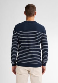 Pulover bleumarin cu dungi orizontale albe, realizat dintr-un material moale. Are un guler rotund și manșete cu nervuri la mâneci și la tiv.