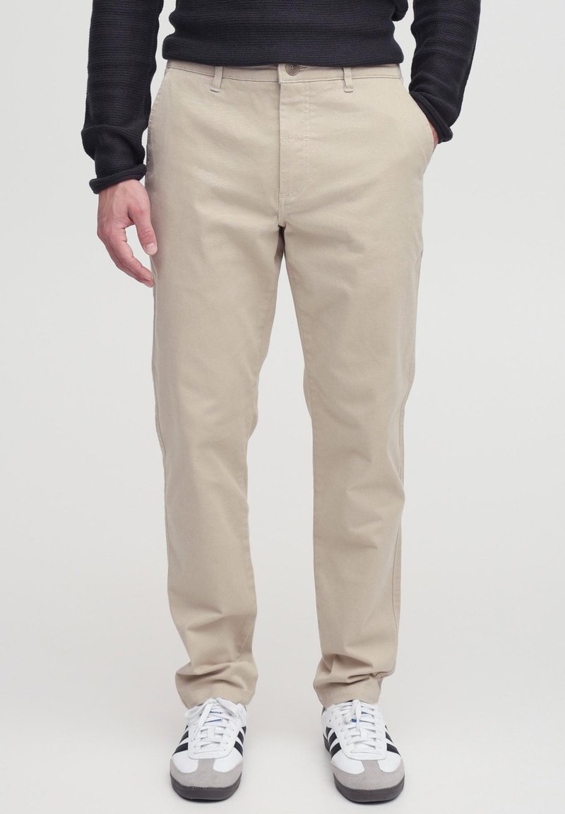 Beige cotton chinos with a straight leg design. Features front pockets and a button closure, paired with gray and white athletic shoes.