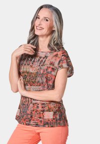 Top a maniche corte multicolore con un motivo astratto nei toni del rosso, arancione e nero, dal taglio comodo e dalla texture liscia.
