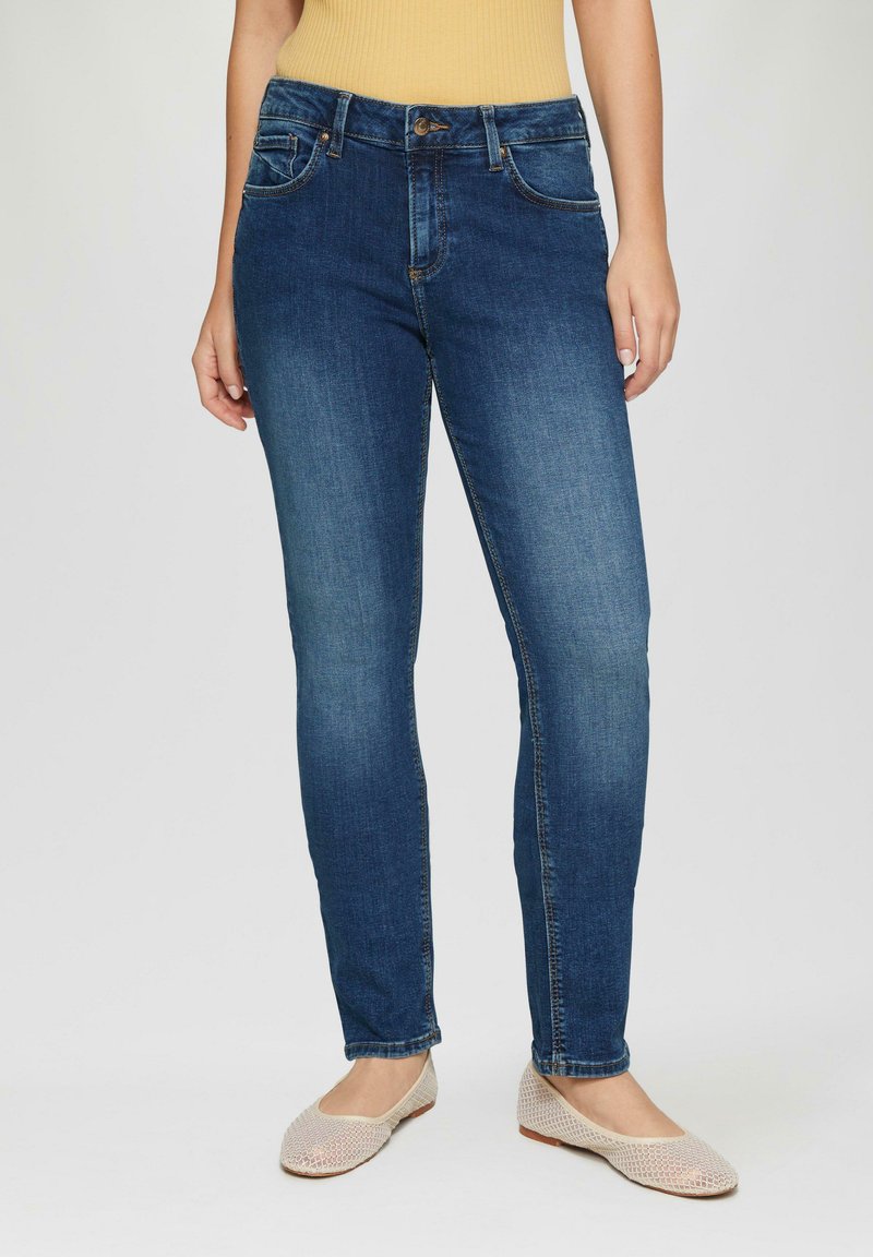 Dunkelblaue Denim-Jeans im Slim-Fit, mit Fronttaschen, einem Knopfverschluss und dezenten Wischdetails. Kombiniert mit beigen Ballerinas.