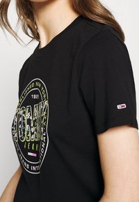 Czarny bawełniany t-shirt z kolorowym nadrukiem kwiatowego logo. Krótkie rękawy z małą naszywką logo na rękawie. Klasyczny design z okrągłym dekoltem.