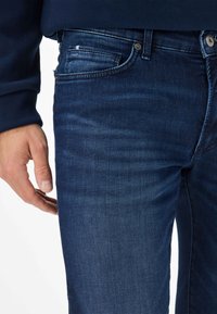 Jeans in denim blu scuro con vestibilità slim, dotati di una tasca frontale, leggera scoloritura sulla coscia e chiusura con bottone in metallo.