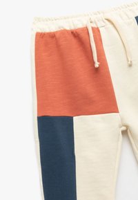 Farveblokerede sweatpants med orange, marineblå og creme sektioner. Lavet af blødt stof med en elastisk talje og snøre.
