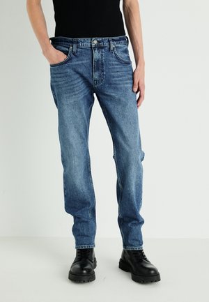 Classic blue denim jeans featuring a straight-leg cut, five pockets, and a washed finish, paired with black lace-up boots.