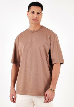 Tricou oversized maro din țesătură de bumbac, cu guler rotund și mâneci scurte. Textură netedă, cusături minime și un croi lejer.