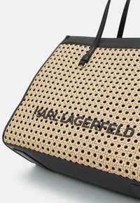 Pletená slaměná taška přes rameno s černými syntetickými doplňky, na přední straně velké logo "KARL LAGERFELD" a pevné dvojité rukojeti.