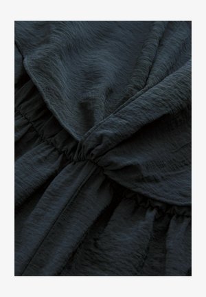 Juodas tekstūruotas audinys su susiraukšlėjimo detalėmis, demonstruojantis minkštus, tekantius drapiravimus ir lengvą blizgesį medžiagoje.