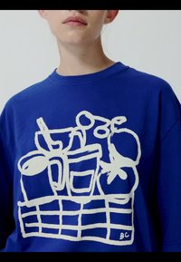 Personne portant une chemise bleue avec un dessin abstrait blanc de lignes représentant des ustensiles de cuisine et des fruits sur le devant.