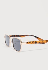 Ορθογώνια γυαλιά ηλίου με χρυστά μεταλλικά πλαίσια και σκοτεινούς φακούς, με μπράτσα σε σχέδιο χελώνας.