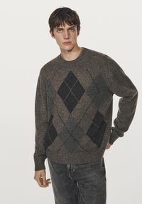 Maglione lavorato a maglia marrone con un motivo argyle testurizzato in grigio scuro e nero. Collo rotondo e polsini a coste. Abbinato a jeans grigi.