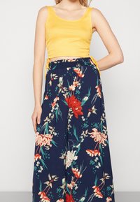 Gul kortärmad topp i kombination med vida marinblå byxor som har ett blommönster i röd, rosa och grön, med en dragsko i midjan.