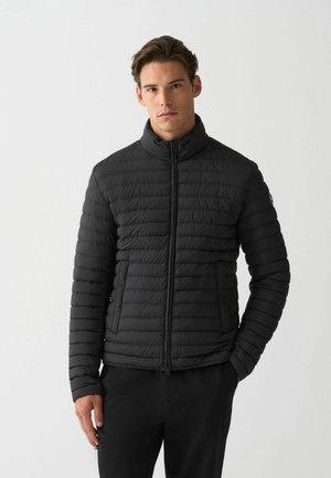 Black puffer jacket with a high collar, zip front, and quilted texture. Features a slim fit and an embroidered logo on the left sleeve.
