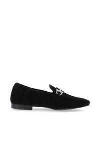 Zapato plano de ante negro con punta afilada, que presenta un detalle de hebilla en tono plateado en la correa y un tacón bajo. Textura suave.