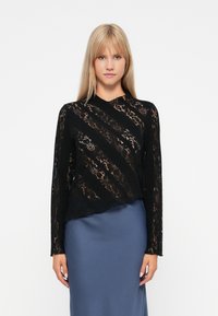 Schwarzes Spitze-Oberteil mit langen Ärmeln, diagonalem Muster, halbtransparenter Textur und hohem Kragen, kombiniert mit einem einfarbigen blauen Satinrock.