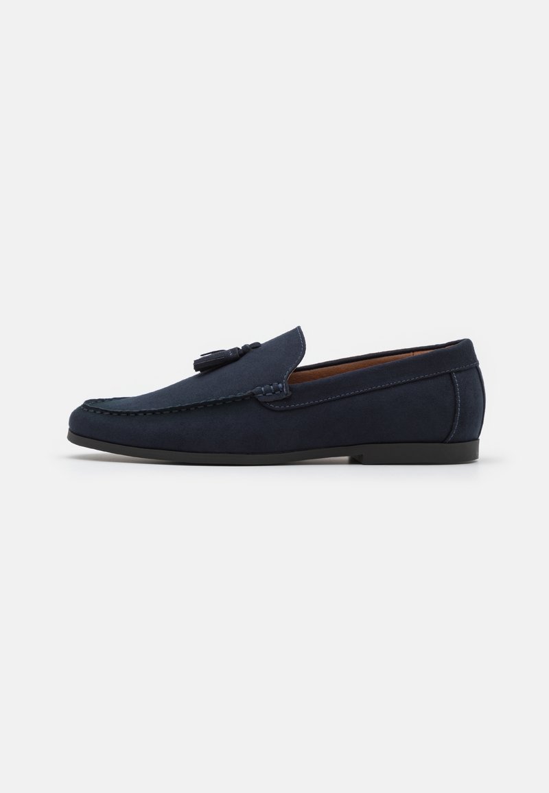 Mocassin pour homme en daim bleu marine avec détail à pampilles, semelle plate noire et coutures visibles le long des bords, présenté en vue de profil.