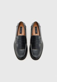 Black leather loafers with stitched detailing, smooth texture, and a rounded toe. Features a tan insole and a slight heel.