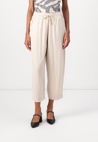 Beige, löst sitzende, cropped Hosen mit elastischem Bund und Kordelzug. Glatte Textur, kombiniert mit schwarzen Absatzschuhen.