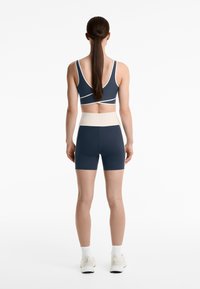 Navy sportbh med vita detaljer, kombinerad med tighta navy-shorts och en ljus midjeband. Modellen har långt brunt hår i en hästsvans.