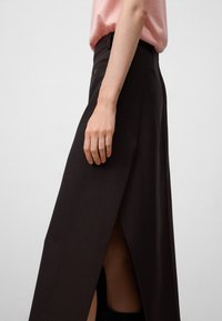 Zwarte hoge taille rok met een zijopening, gemaakt van textuurstof. Aangevuld met een strak ontwerp en minimale stikdetails.