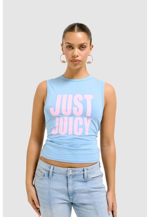 Lichtblauwe mouwloze crop-top met "JUST JUICY" in vet roze letters. Zachte katoen materiaal. Gecombineerd met lichtblauwe spijkerbroeken.