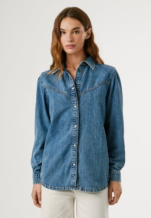 Chemise en denim de couleur bleu clair avec une fermeture à boutons classique, un col pointu et des détails en forme de yoke de style western. Manches longues et coupe ajustée.