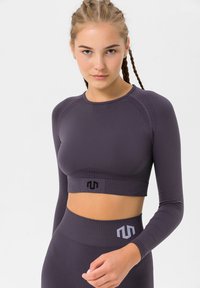 Purple long-sleeve cropped athletic top with ribbed texture, black logo at the hem, and breathable pattern on the shoulders.