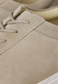 Zapatillas de ante beige con parte superior texturizada, cordones planos y suela de goma blanca. Presenta detalles de costura a lo largo de las costuras para mayor durabilidad.