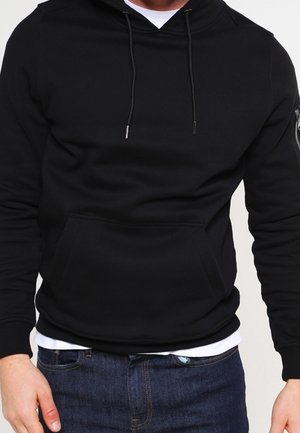 Sweat-shirt à capuche noir avec une poche kangourou à l'avant, des cordons de serrage et une poche zippée sur le côté. Fabriqué en tissu en coton mélangé doux.