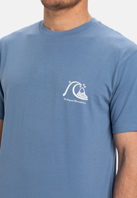 Blauwe katoenen T-shirt met een witte golfafbeelding van een vulkaan, korte mouwen en een ronde hals. Zachte textuur, casual pasvorm.