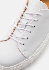 Sneaker bianca in pelle con punta tonda, lacci bianchi piatti, dettagli beige e suola in gomma testurizzata con grip a motivo. Finitura liscia.