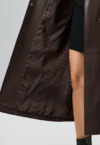 Bruine leren jas met een voering met stippenpatroon. Het interieur heeft ronde ontwerpen in verschillende tinten bruin.