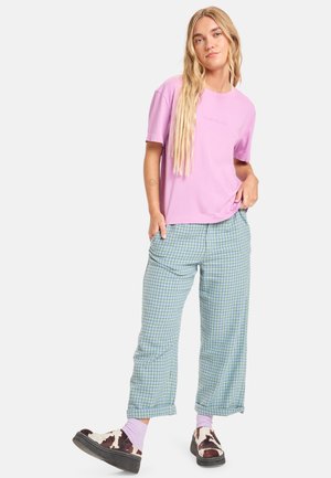 Pink cotton t-shirt, relaxed fit. Light blue checkered pants with a loose cut. Brown shoes with a cow print design and pink socks.