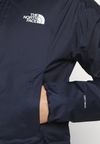 Men's navy jacket features a zippered pocket, elastic cuffs, and "DRYVENT" branding, made from water-resistant material.