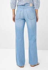 Pantalones vaqueros de mezclilla azul claro de corte acampanado con cintura de altura media, dos bolsillos traseros y una etiqueta de marca en la cintura.