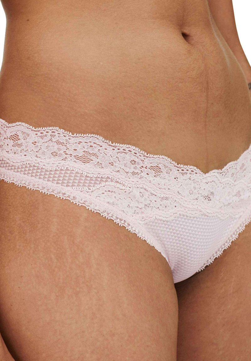 Tanga de encaje rosa con un patrón texturizado. La cinturilla presenta un intrincado detalle de encaje floral, realzando el diseño delicado.