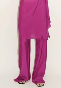 Fuchsia twee-delige outfit met een losse, doorzichtige top en wijde broekspijpen. De stof lijkt licht van gewicht met een gladde textuur. Zwarte sandalen zijn inbegrepen.