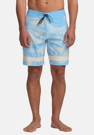 Costumi da bagno leggeri blu chiaro da uomo con motivi astratti beige e un cordoncino nero, indossati a piedi nudi su uno sfondo neutro.