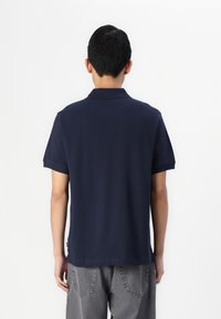 Jūras zilas krāsas polo krekls ar īsām piedurknēm un apkakli, izgatavots no gludas auduma. Veidots ar taisnu apakšmalu un minimālu dizainu.