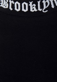 Tessuto nero a maglia con texture a coste, caratterizzato dalla parola "Brooklyn" ricamata in bianco con un font gotico lungo il margine superiore.